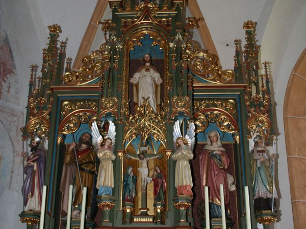 Der Altar der Walfahrtskirche zu den Hl. Chrysanth und Daria - ein verzierter Hochaltar mit Christusfigur, Heiligenstatuen, Kerzen und goldenen Ornamenten.