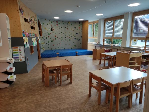 Im Vordergrund sind drei Kindertische mit jeweils vier Kinderstühlen zu sehen, im Hintergrund ist eine Kletterwand für die Kinder