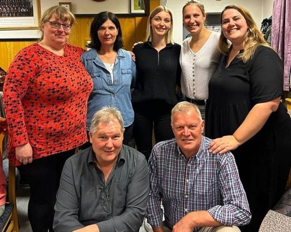 Eine Gruppe von sieben Personen posiert gemeinsam in einem gemütlichen, schwach beleuchteten Innenraum und vermittelt eine freundliche Atmosphäre